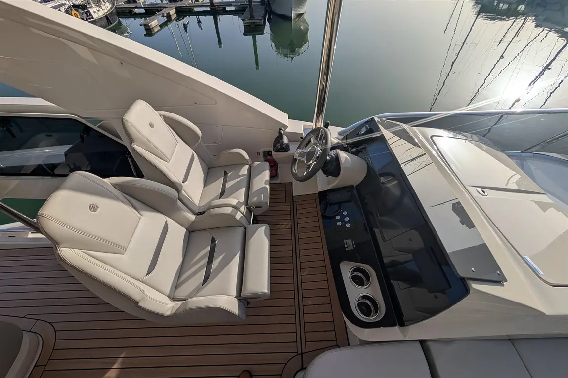 Modern boat cockpit featuring two cream seats, steering wheel, control panel, and reflections in calm water.